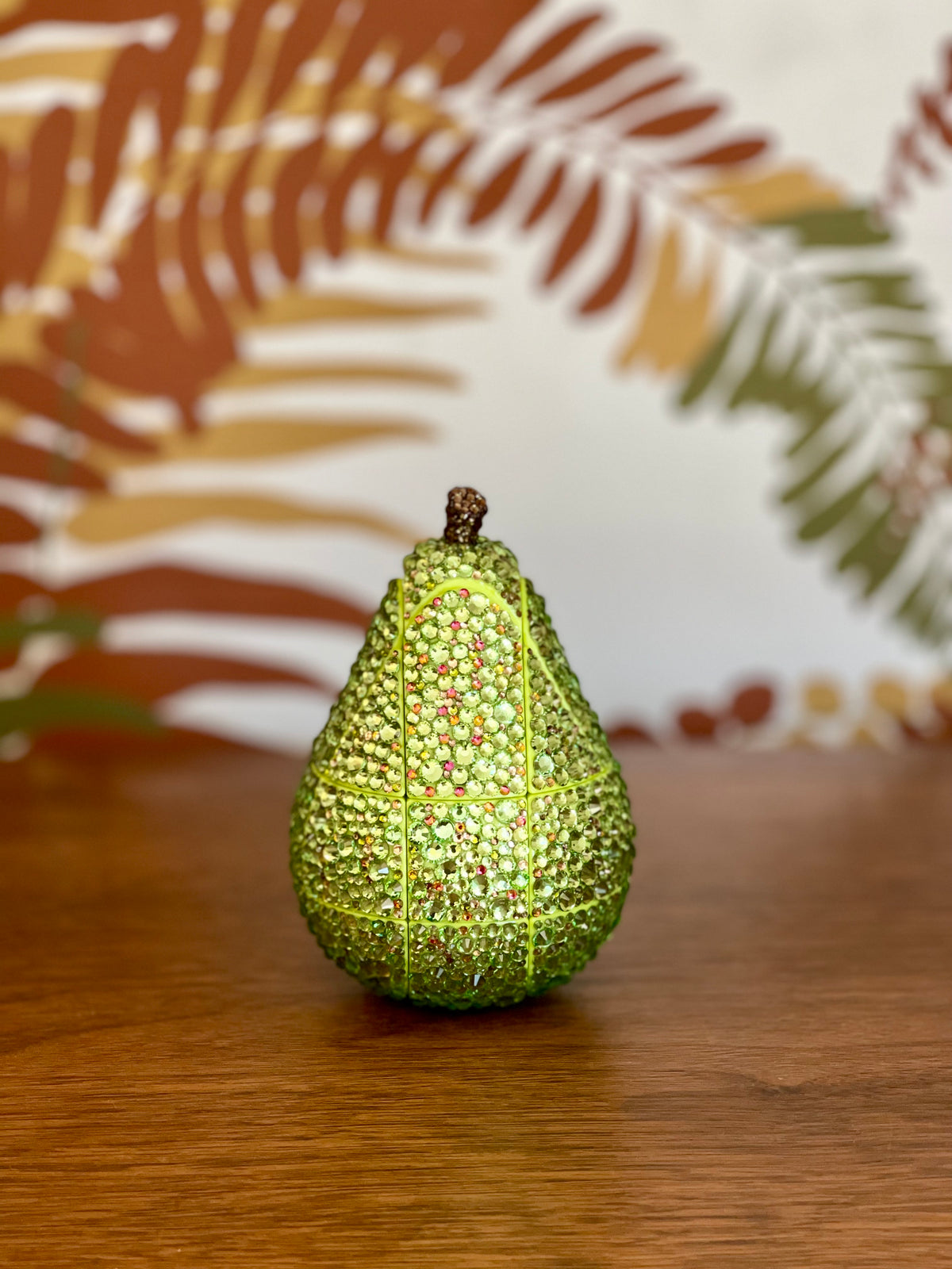 Decorative green pear shaped puzzle cube with custom Looking Glass Gems rhinestone gemstone-like embellishments on a wooden surface with a patterned fabric background.